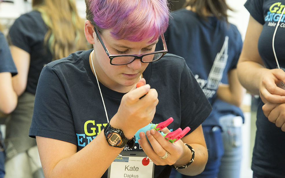 Camper with purple hair working on robotic hand with a tool.