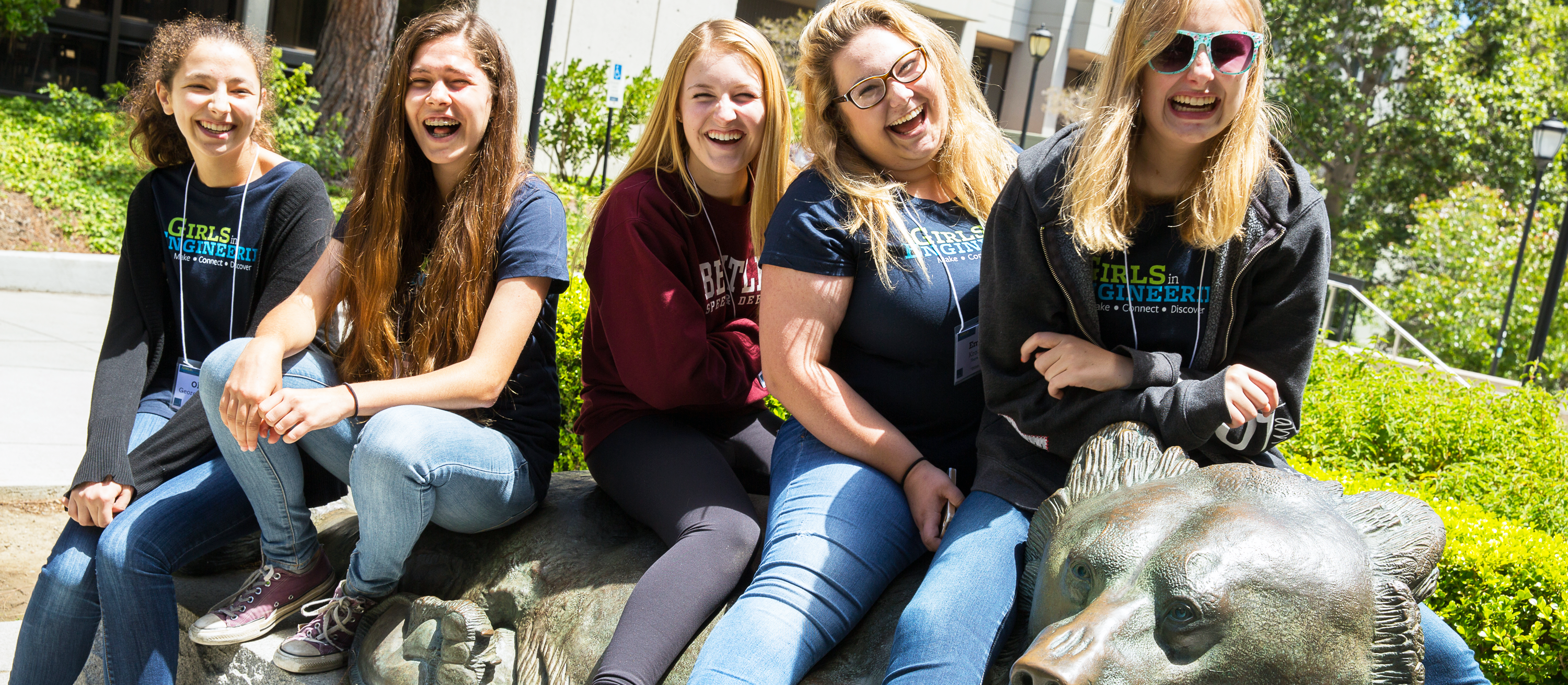 five young adults laughing sitting on a UC Berkeley Bear statue.